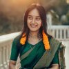 A young woman in a green saree with floral adornments, outdoors during sunset.